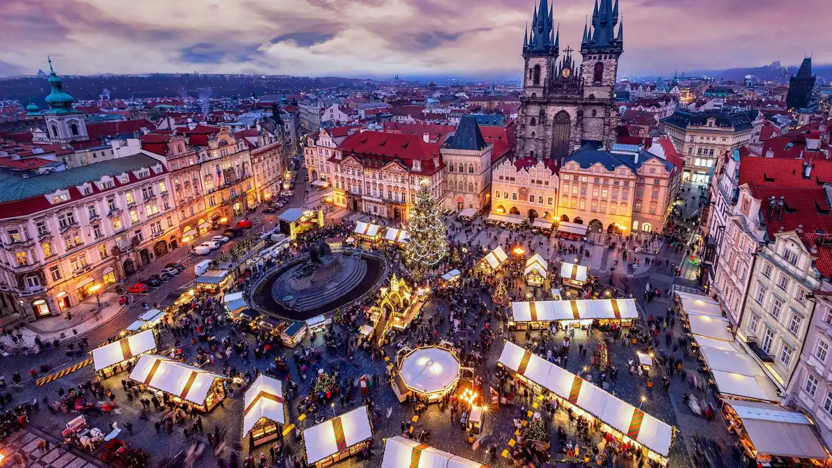 A guide and visitors beside lit Christmas market stalls in Prague's Old Town Square