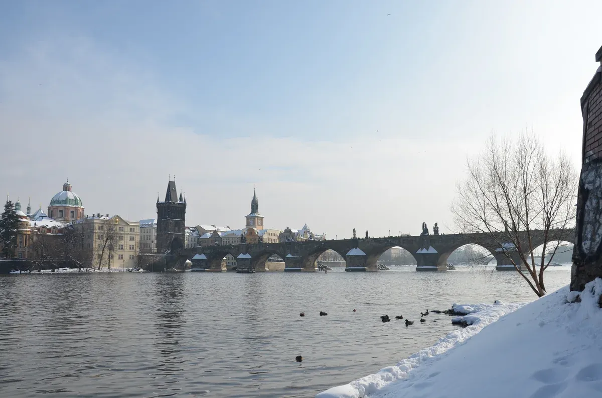 Charles Bridge and the Old Town Bridge Tower over the Vltava with snow on the riverbank