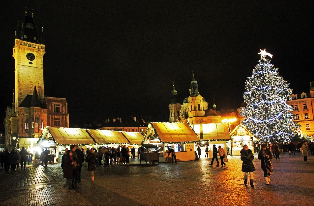 Old Town Square Christmas market stalls glowing under the Old Town Hall tower and the big tree at night