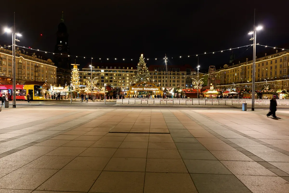 The Dresden Christmas market on the Altmarkt at night, with the tree and the Striezelmarkt arch lit at the far end of the square