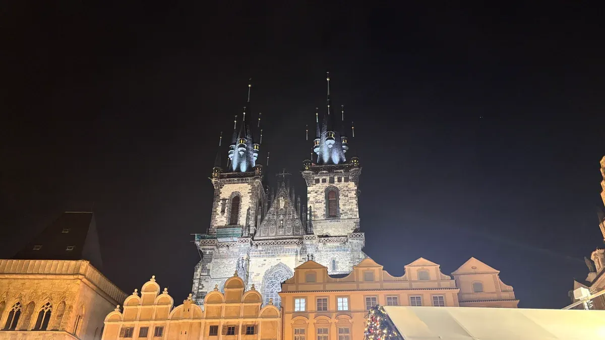 Týn Church floodlit above the Old Town Square rooftops at night